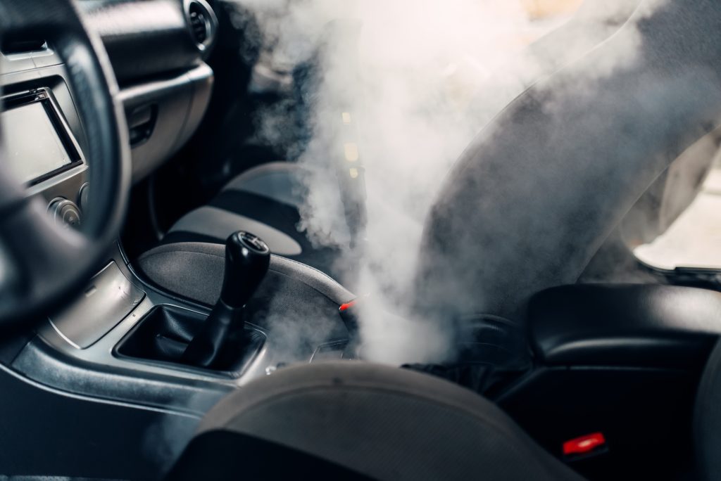 Detailing expert using high-temperature steam cleaner on car dashboard and vents for sanitization.