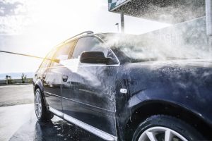 Mobile car detailer working in a residential driveway, cleaning a vehicle with basic tools and limited setup