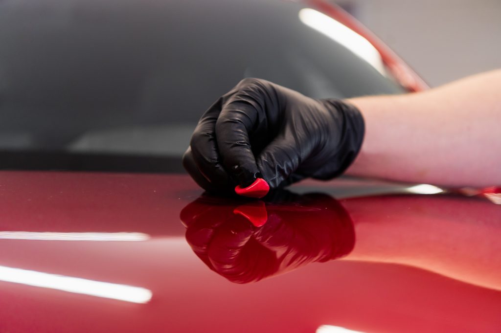 Technician performing Clay Bar treatment on red car at CarZone Auto Detailing in Burlington